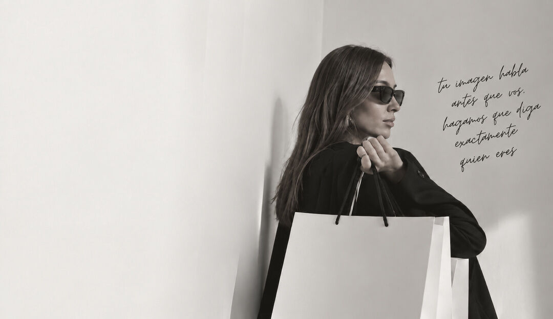 Pia con anteojos de sol y una bolsa de compras junto a una frase en la pared